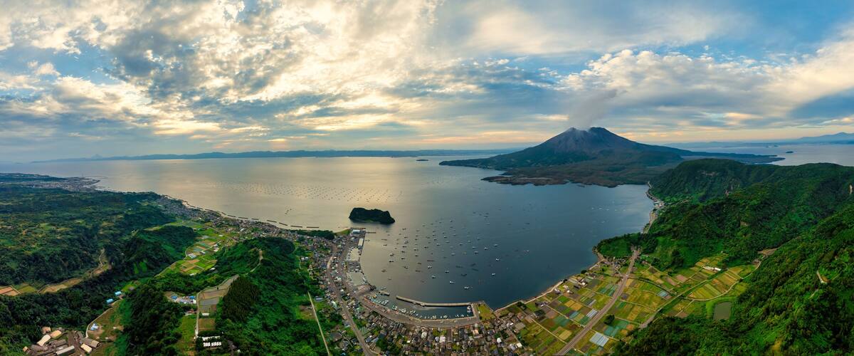 A coastal town with a large body of water, a mountain, and lush green hills.