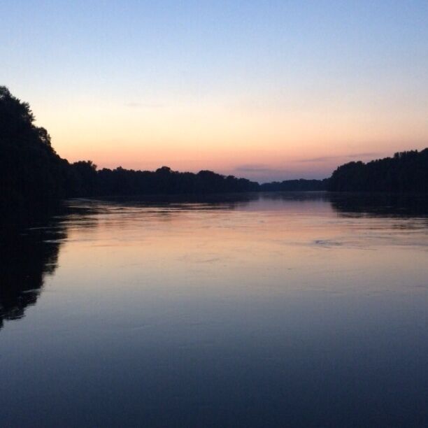 A calm river at dusk with a forested bank.