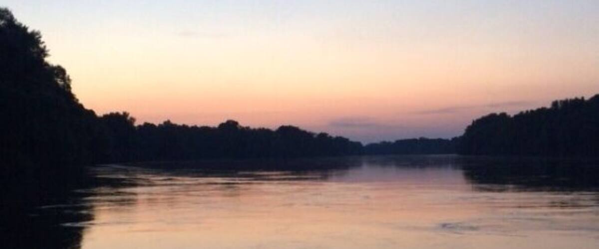 A calm river at dusk with a forested bank.