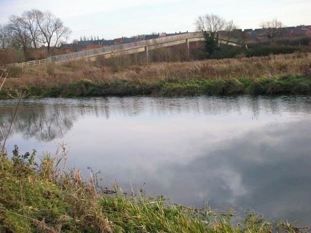Footbridge below Higham Ferrers. The footbridge carries Kings Meadow Lane over the A45 bypass, giving access to the riverside paths, old gravel pits and the footpath to Irthlingborough. The River Nene (pronounced 'Nen' hereabouts) is in the foreground.