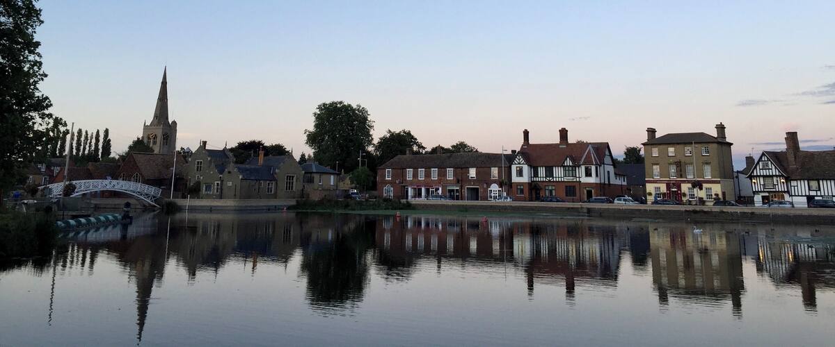A calm river reflecting buildings and a church spire.