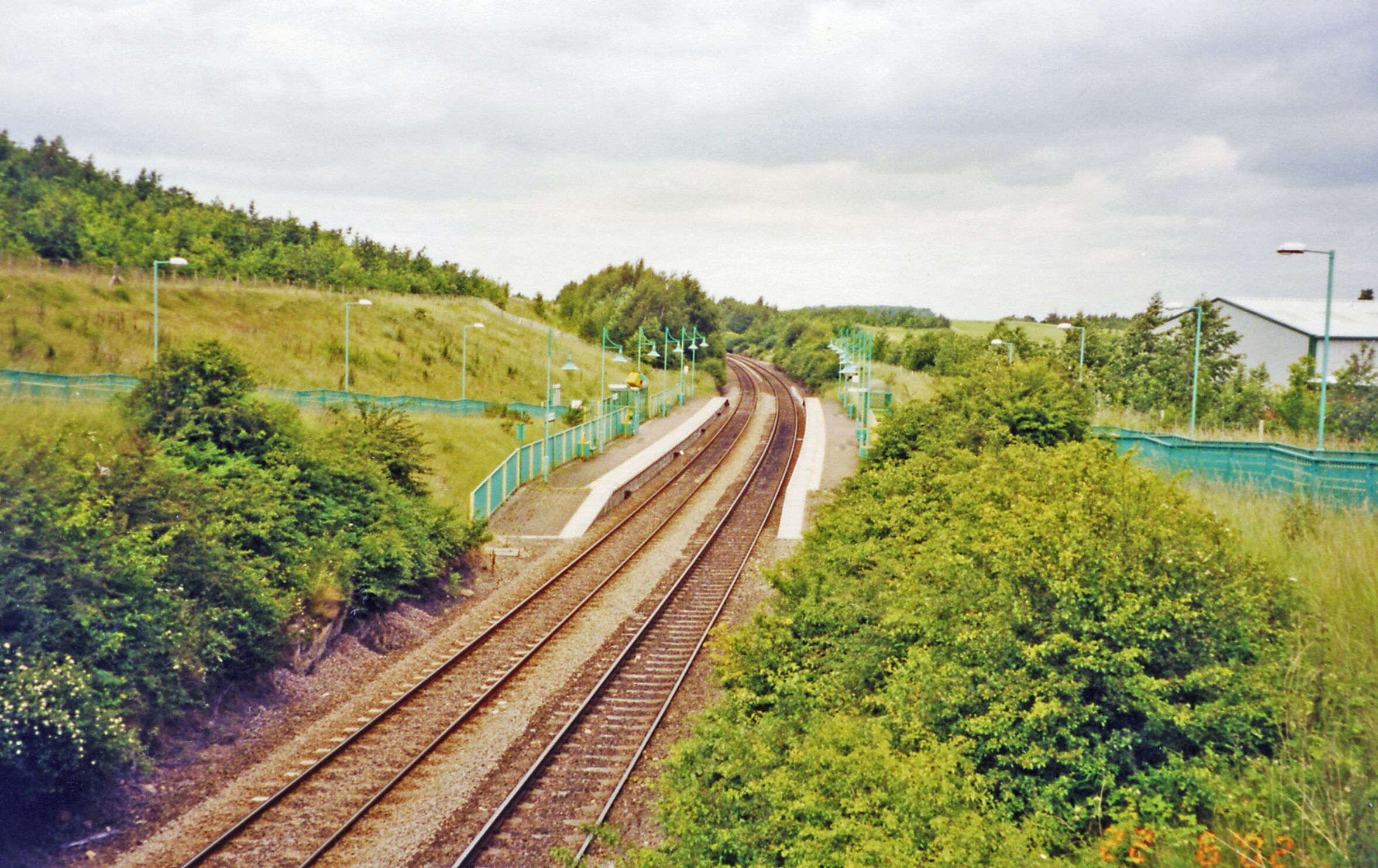Railway tracks curving through a green landscape with trees and a fence.