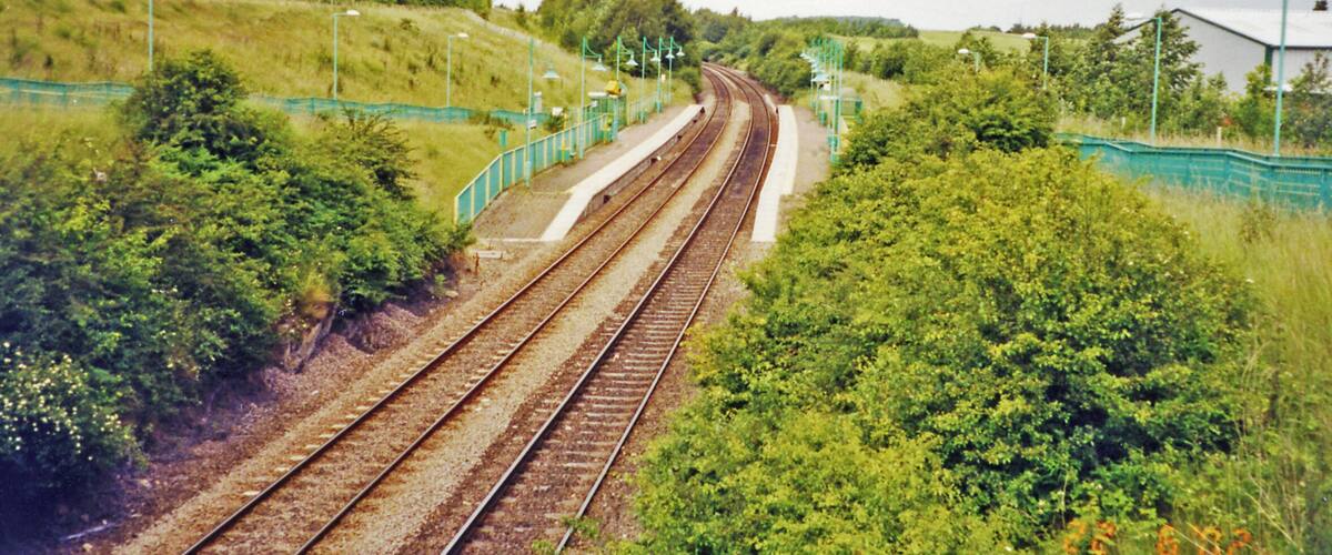 Railway tracks curving through a green landscape with trees and a fence.
