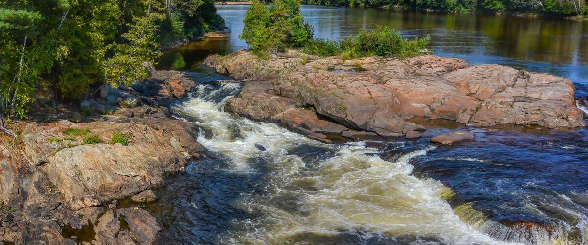 A river flowing through a rocky landscape with dense green trees and a clear blue sky.