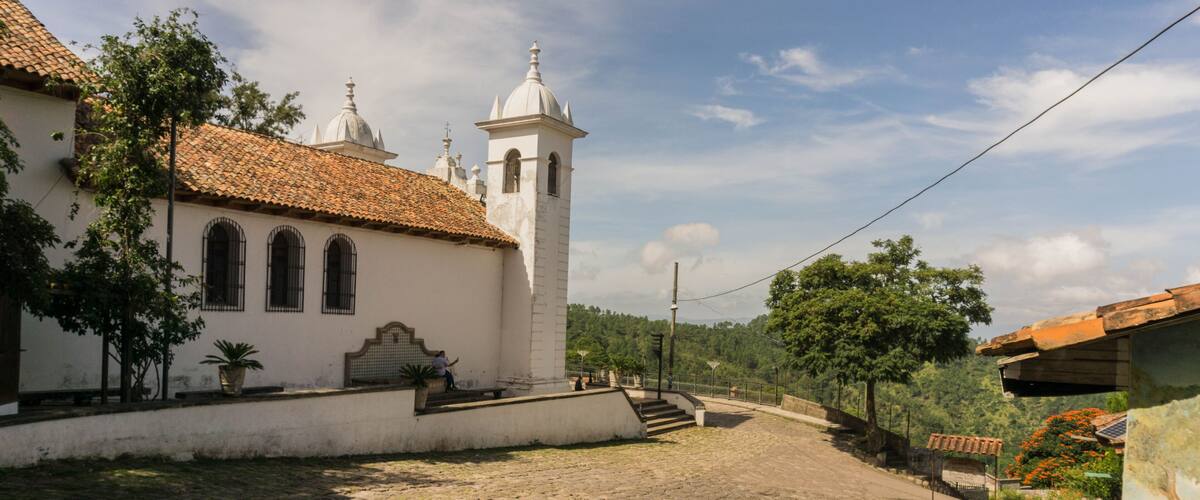A cobblestone street leading to a white church with a bell tower.