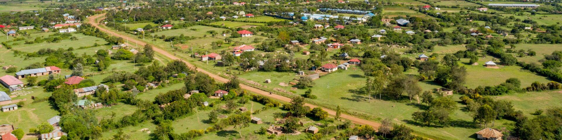 Aerial view of a picturesque rural village with homes and lush greenery under a sunny sky, Muhuru, Kenya.