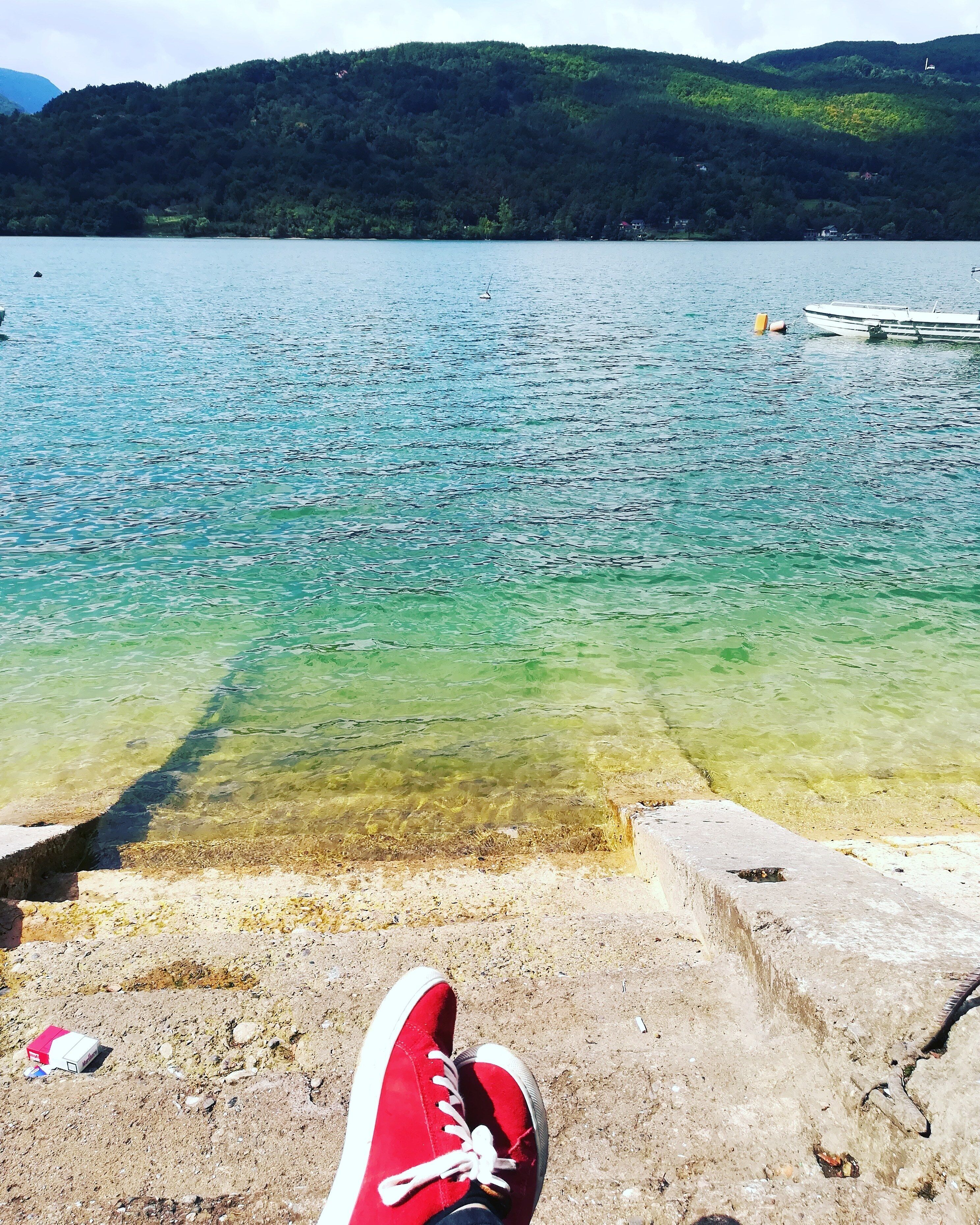 A lake with clear water, a concrete dock, and a red shoe on the shore.
