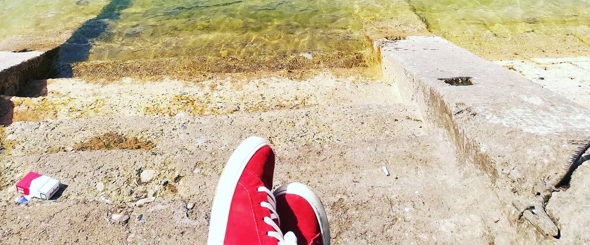 A lake with clear water, a concrete dock, and a red shoe on the shore.