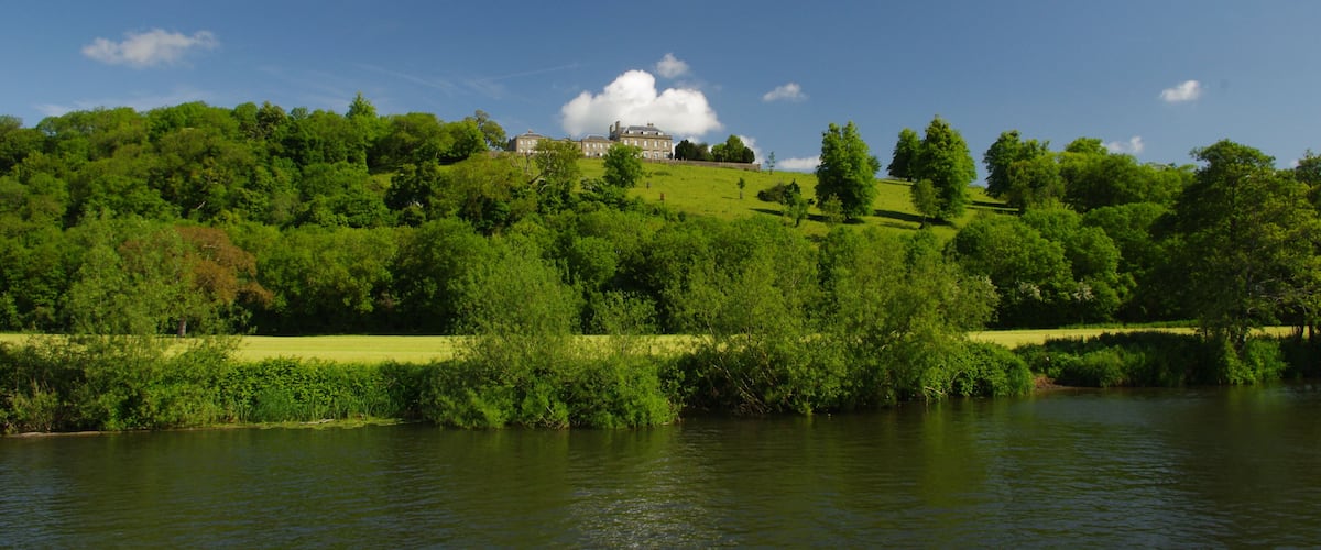 A large house on a hill with a river in the foreground.