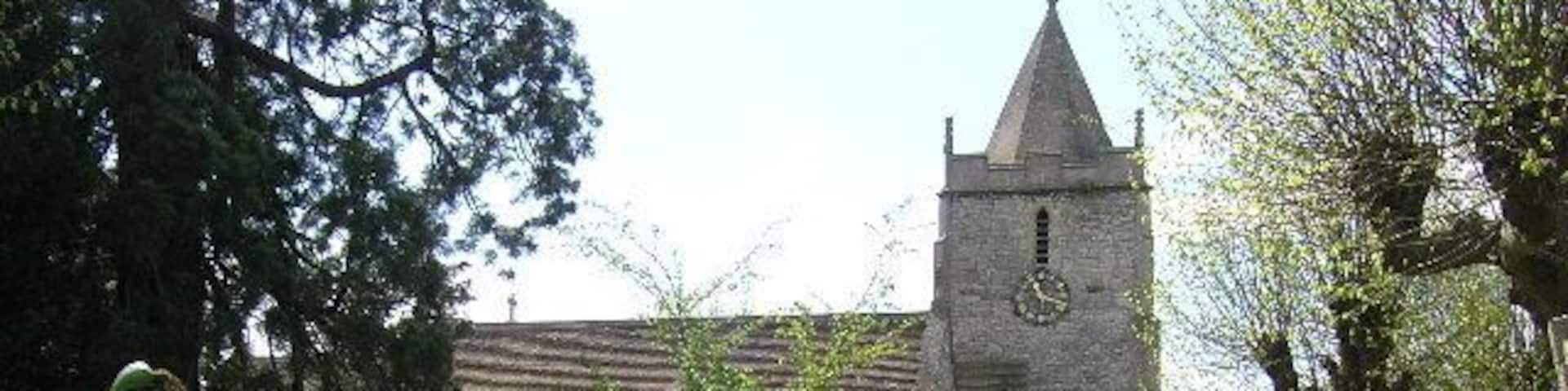 A church with a tall tower and a clock, surrounded by a cemetery with gravestones and lush greenery.
