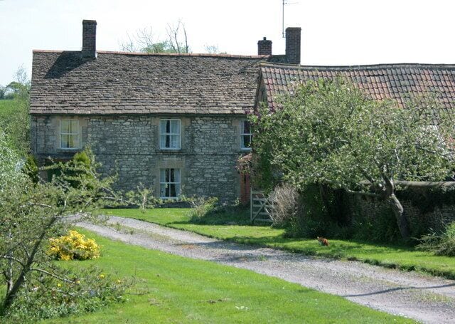 A stone house with a tiled roof, surrounded by a grassy garden and a gravel path.