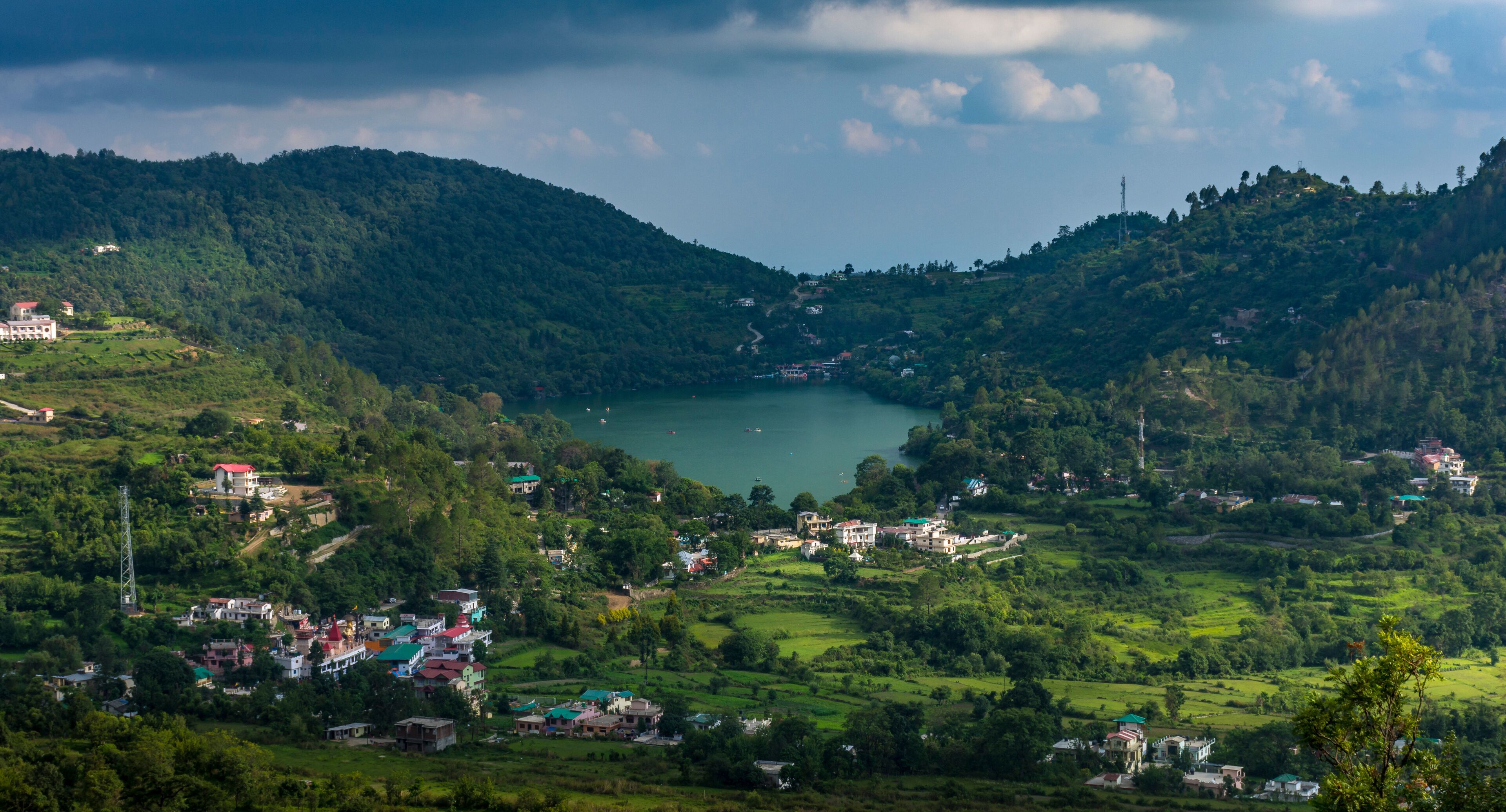 A mountainous landscape with a lake surrounded by greenery and scattered buildings.
