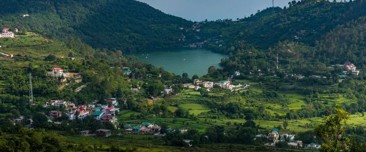 A mountainous landscape with a lake surrounded by greenery and scattered buildings.