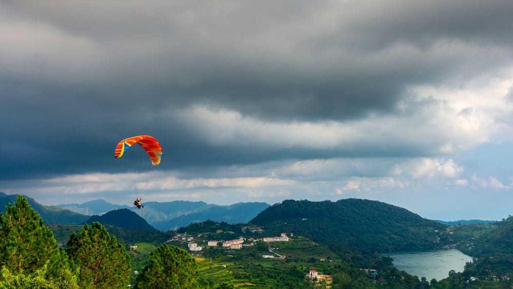 A paragliding scene over a mountainous landscape with a lake and buildings.