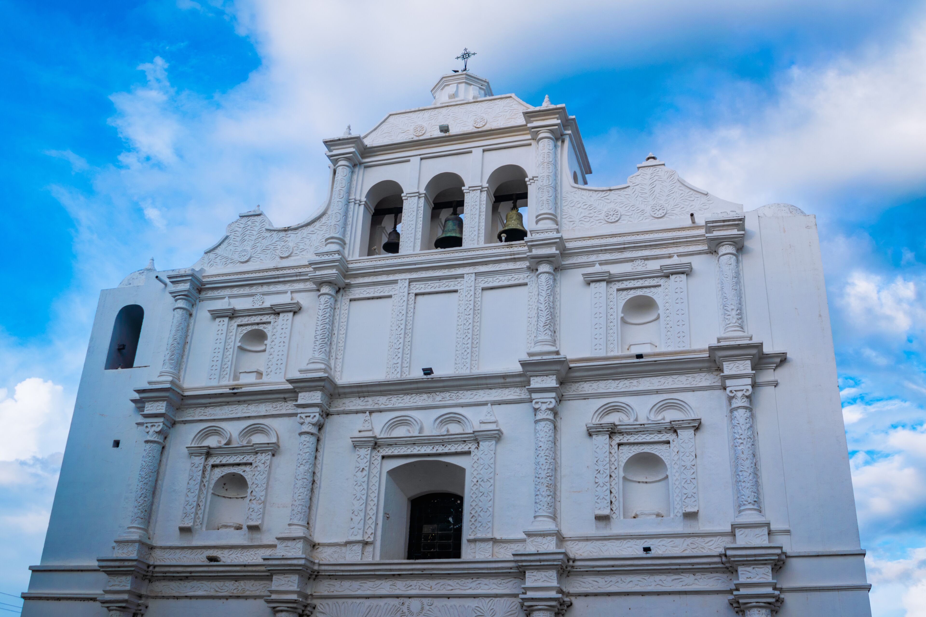 A white church with ornate carvings and three visible bells.