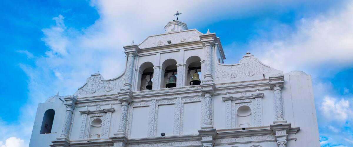 A white church with ornate carvings and three visible bells.