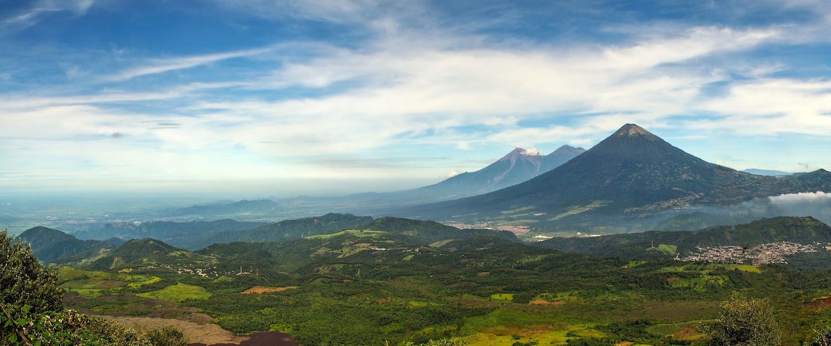 A mountainous landscape with a prominent peak, lush green valleys, and a distant town.