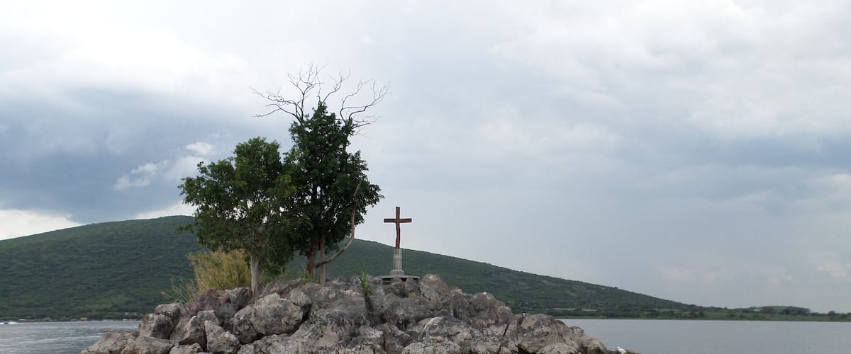 A rocky island with a cross and a tree in a body of water.