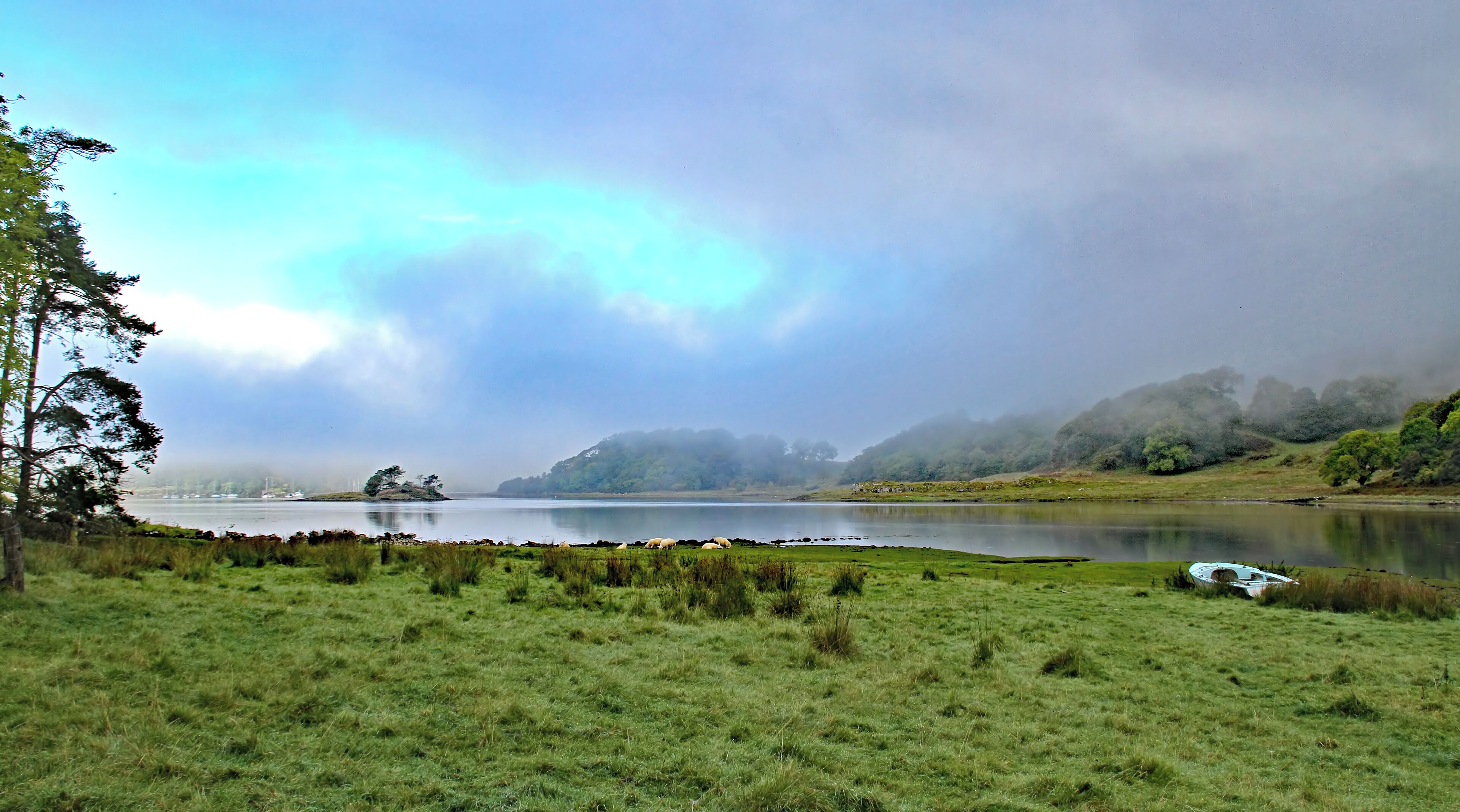 A calm lake surrounded by grassy fields and trees, with a boat on the shore.