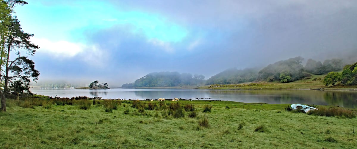 A calm lake surrounded by grassy fields and trees, with a boat on the shore.