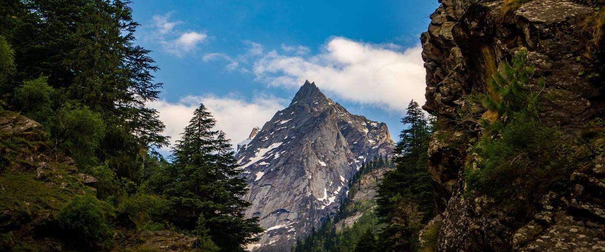 A mountain peak surrounded by dense forest and rocky cliffs.