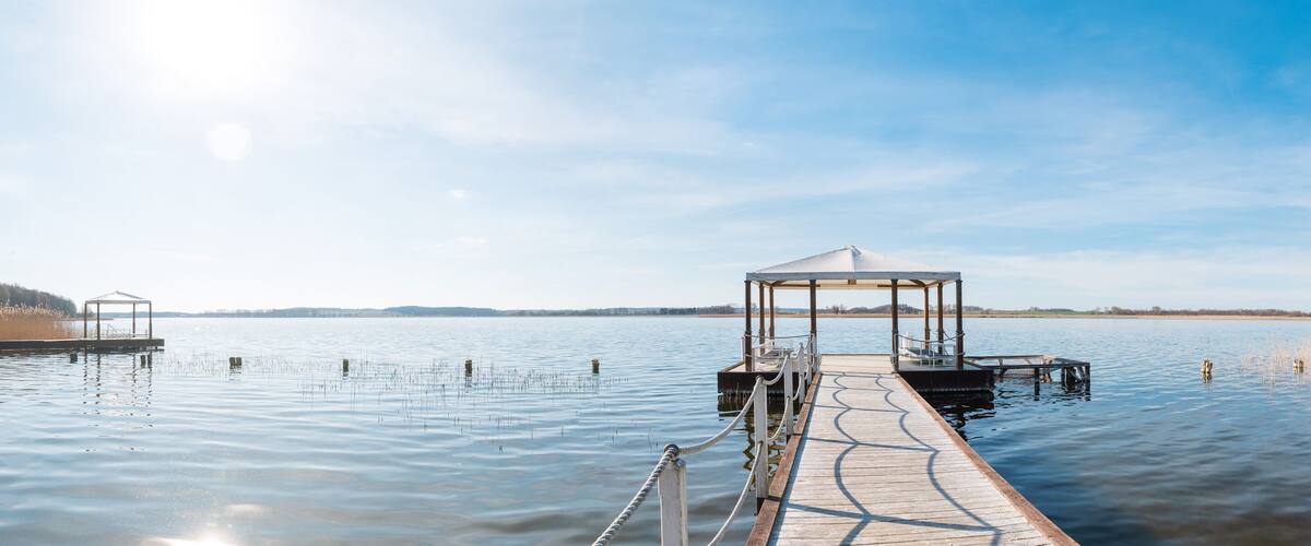 A wooden pier extending into calm water with a covered gazebo at the end.