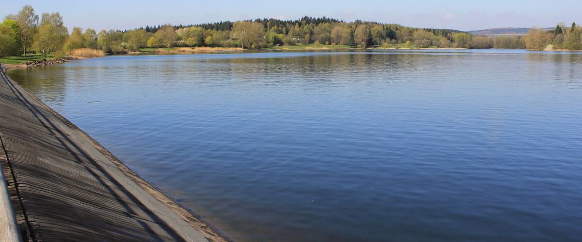 A calm lake with a wooden dock on the left, surrounded by trees and hills in the background.