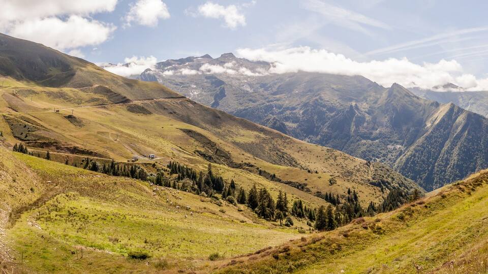 A mountainous landscape with a winding road, a small building, and a forested valley.