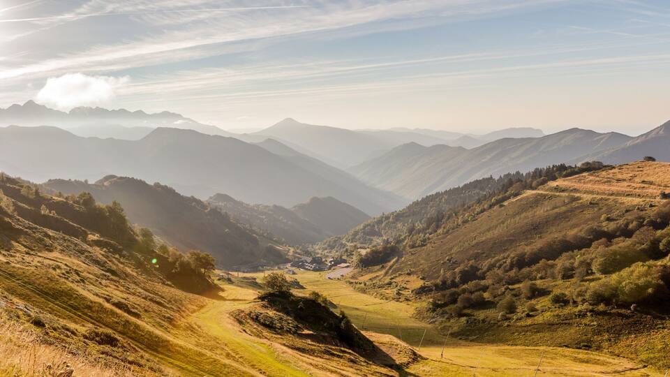 A mountainous landscape with a valley, a dirt road, and a ski lift.