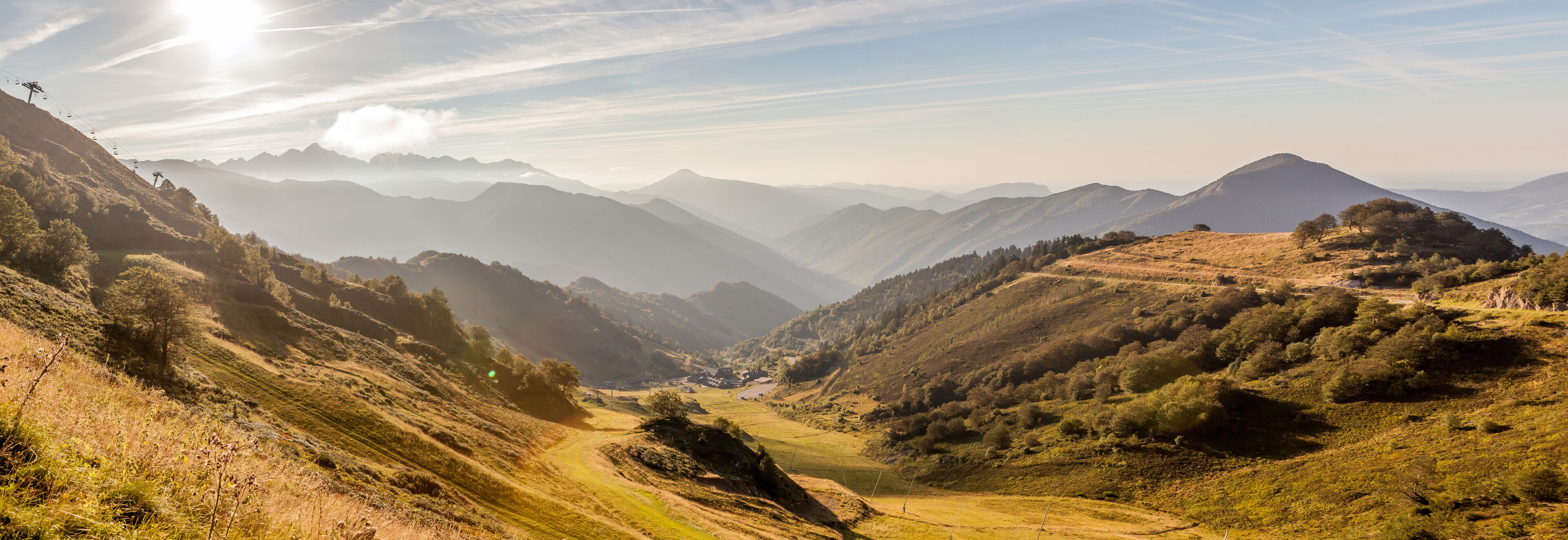 A mountainous landscape with a valley, a dirt road, and a ski lift.
