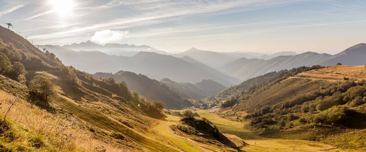 A mountainous landscape with a valley, a dirt road, and a ski lift.