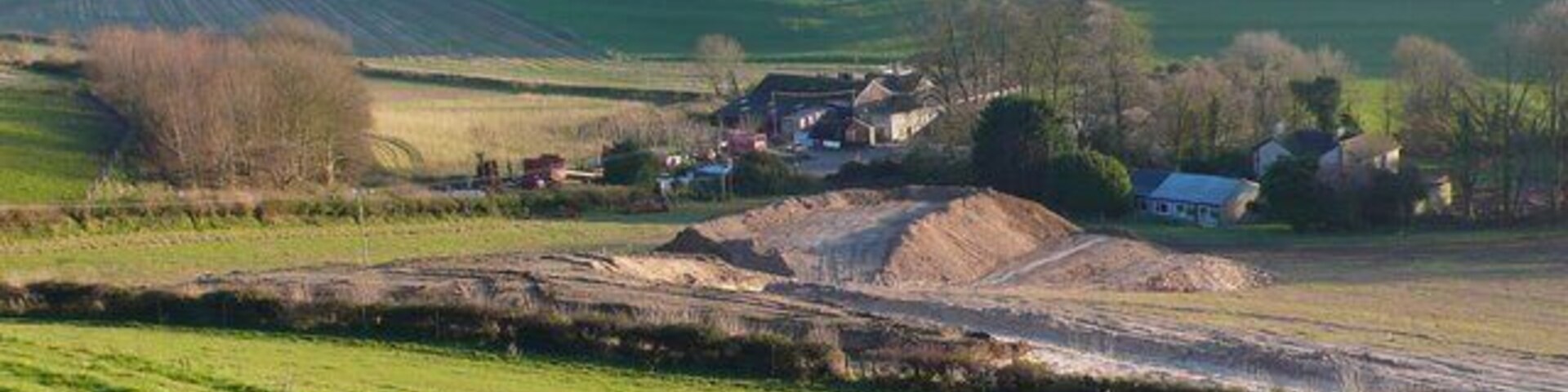A rural landscape with rolling hills, a dirt road, and a small cluster of houses.