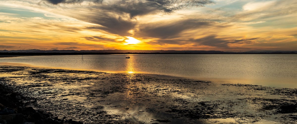 A sunset over a calm body of water with a beach in the foreground.