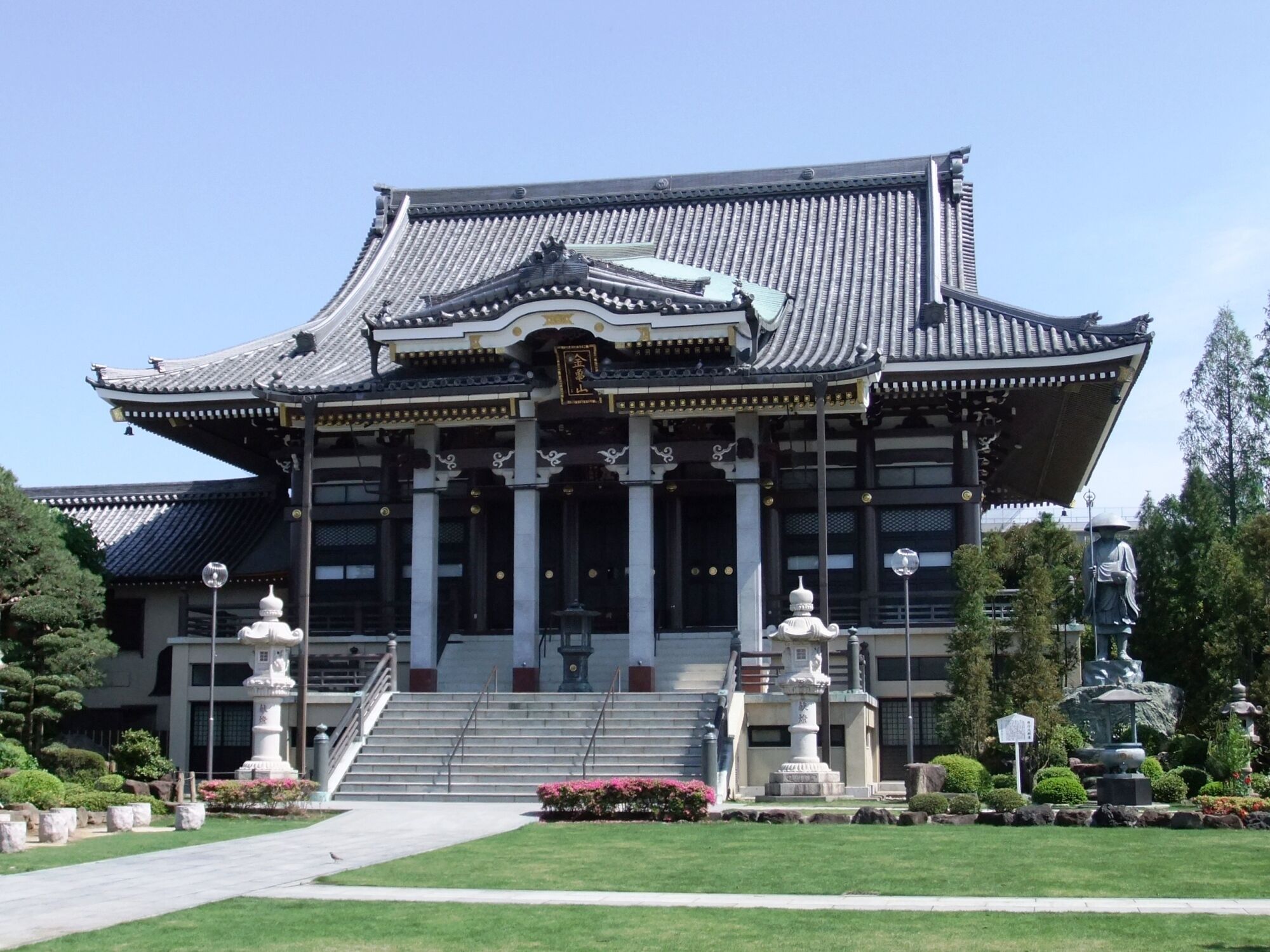 A traditional Japanese building with a tiled roof, columns, and statues.