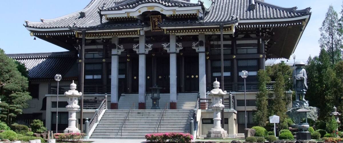 A traditional Japanese building with a tiled roof, columns, and statues.