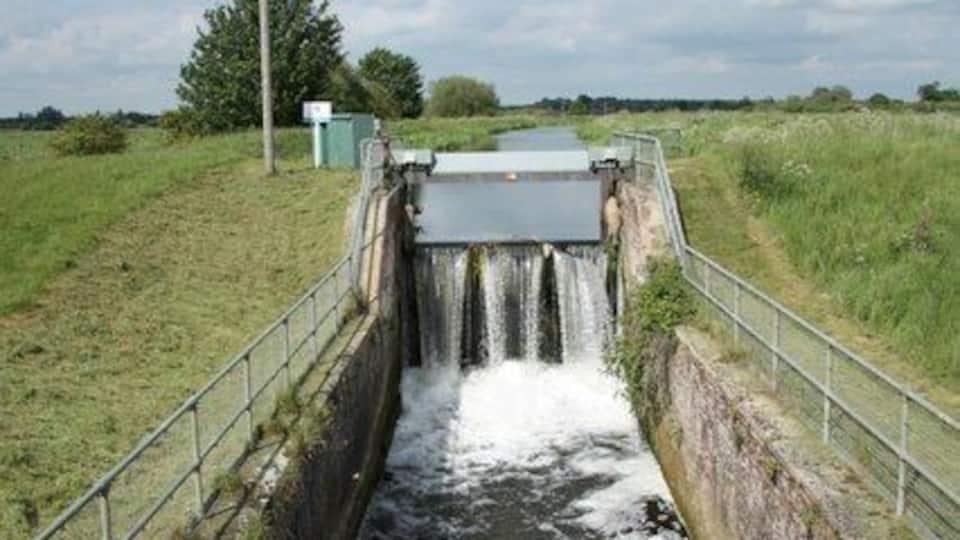 A narrow water channel with a concrete wall and metal railing, leading to a small waterfall.