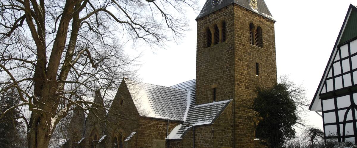 A historic church with a tall tower, snow-covered ground, and a leafless tree.
