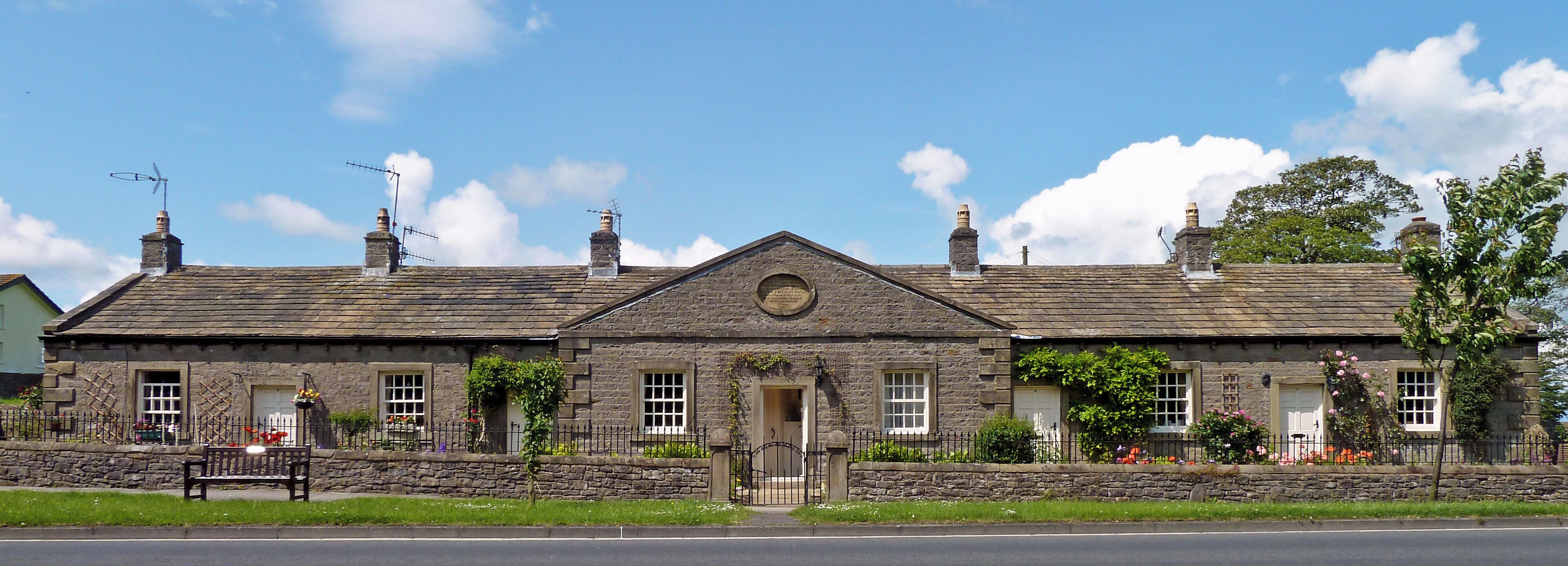 A stone building with a gabled roof, a central door, and multiple chimneys.