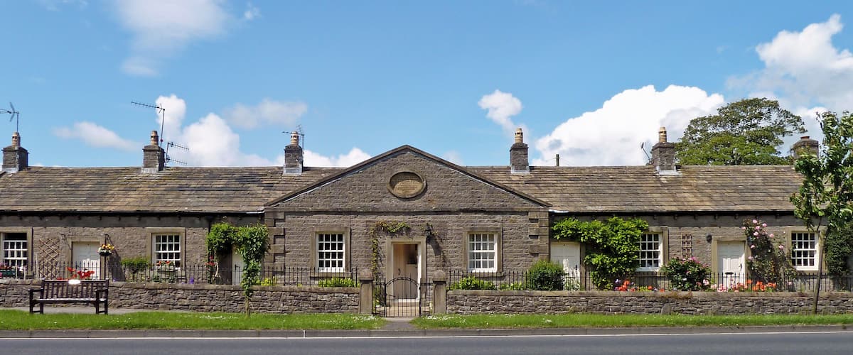 A stone building with a gabled roof, a central door, and multiple chimneys.
