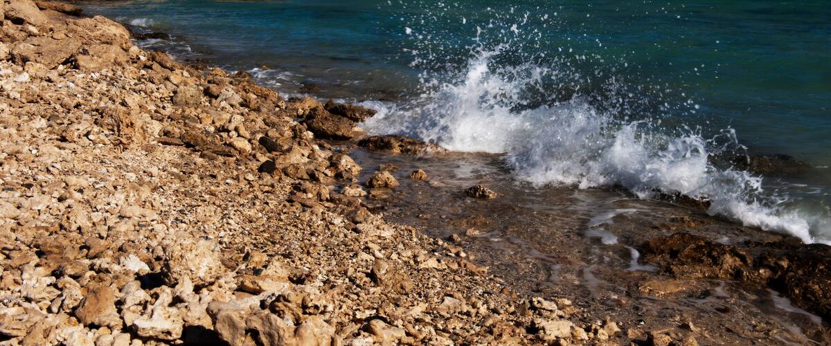 A rocky shoreline with waves crashing onto the beach and a clear blue sky.