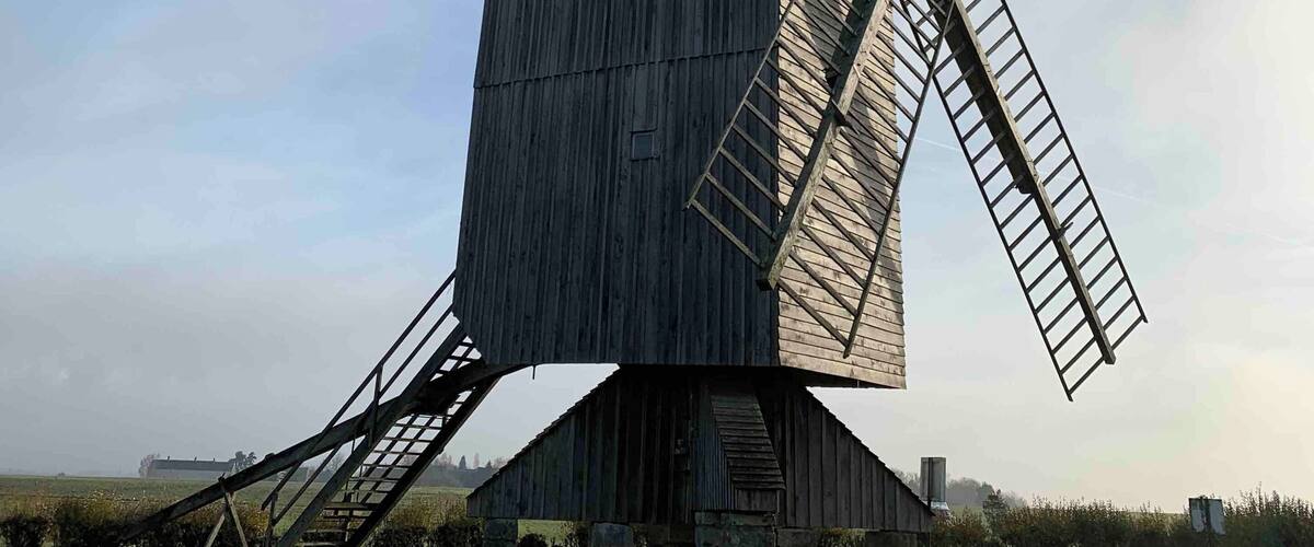 A large wooden windmill with a tall, narrow tower and large sails.