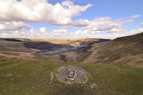Une vallée où se dresse un monument de pierre, entourée de collines verdoyantes, et une ville visible au loin.