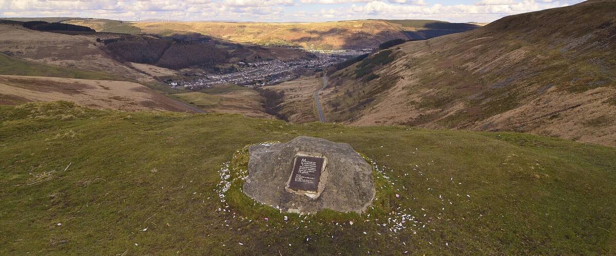 A valley with a stone monument surrounded by grassy hills and a town in the distance.