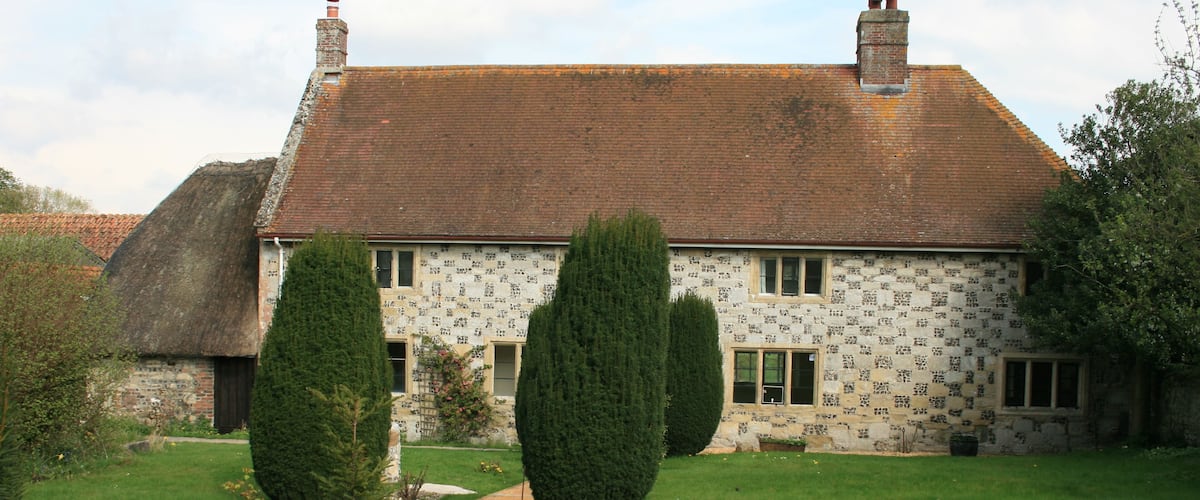 A traditional house with a tiled roof, a thatched roof structure to the left, and a well-maintained lawn with two trimmed trees.