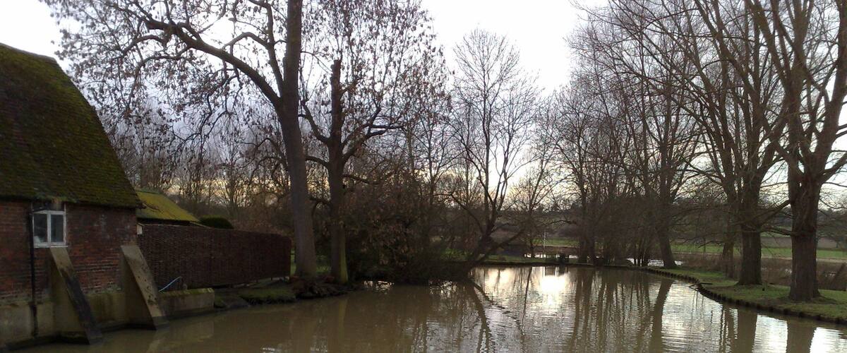 A flooded river with reflections of trees and a brick building.