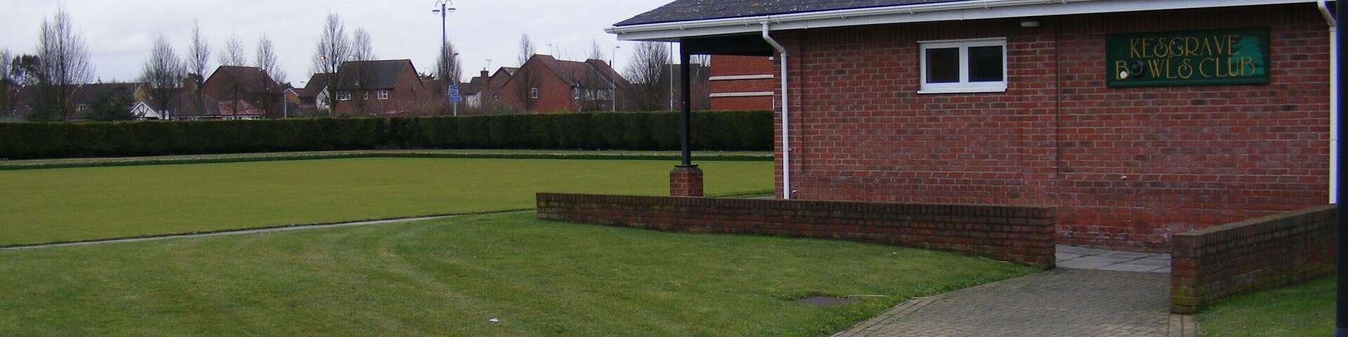 A brick building with a sign reading "Kegrave Bowling Club" in front of a green field.