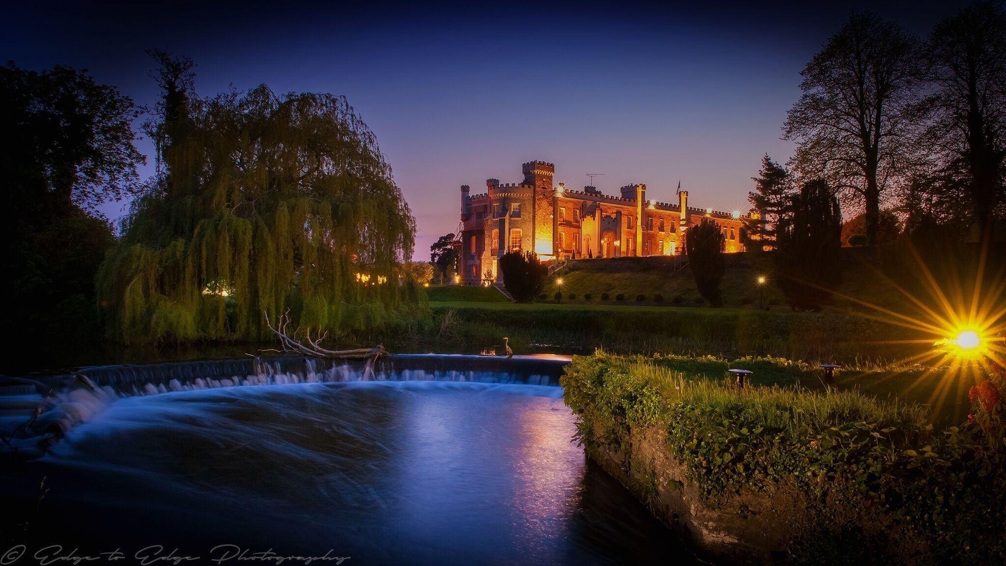 A castle at dusk with a flowing river in the foreground.