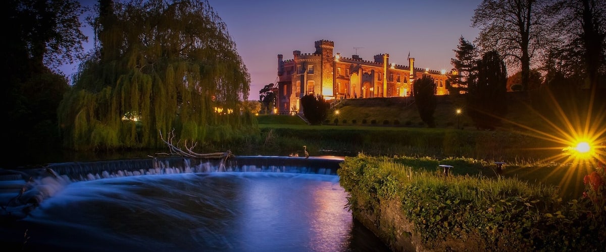 A castle at dusk with a flowing river in the foreground.