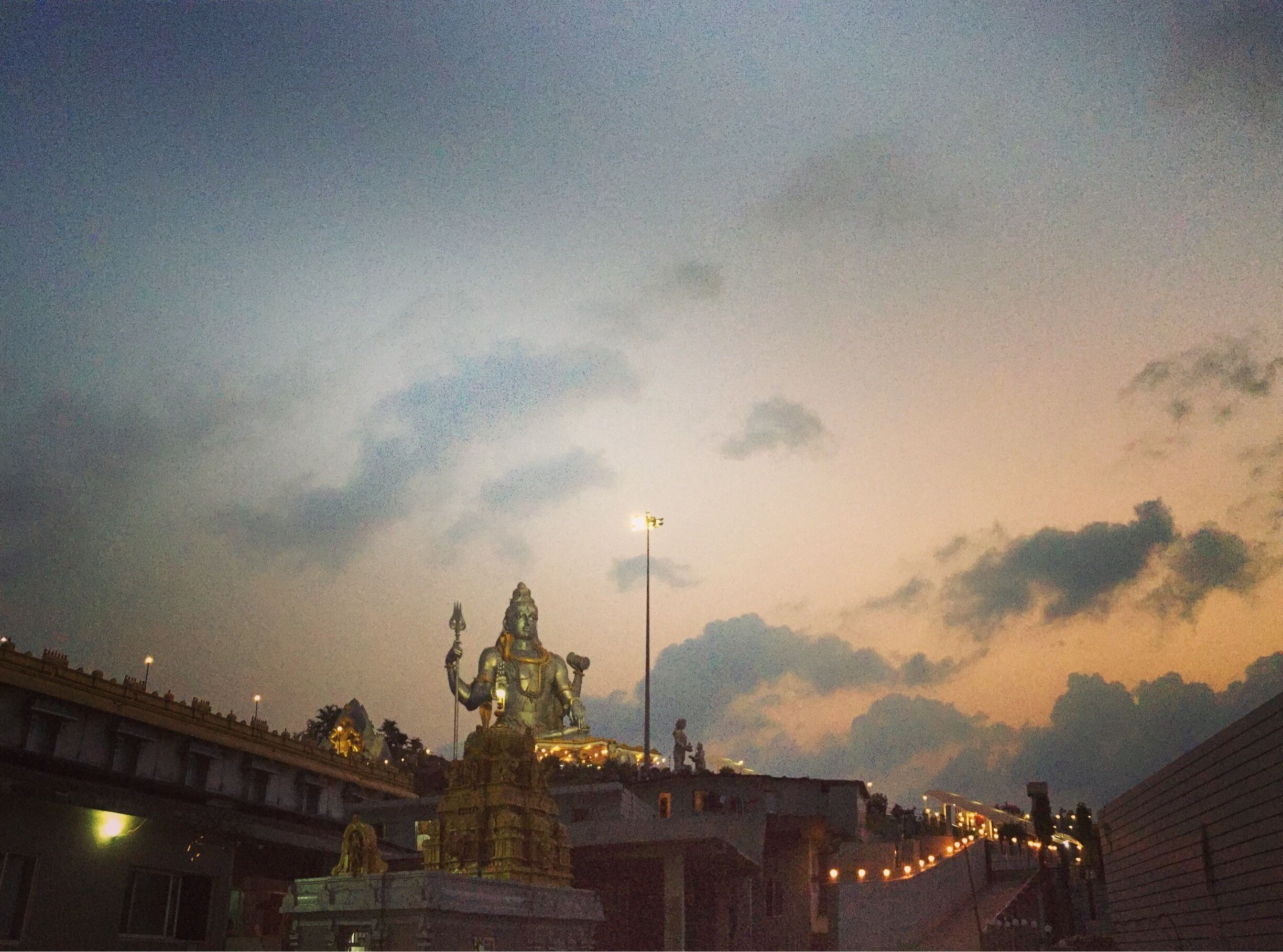 A statue of a deity on a temple platform with a bridge in the background.