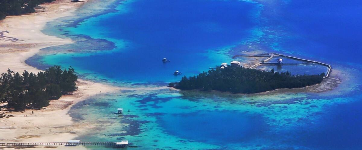 An aerial view of a turquoise lagoon with a small island, a pier, and a boat.